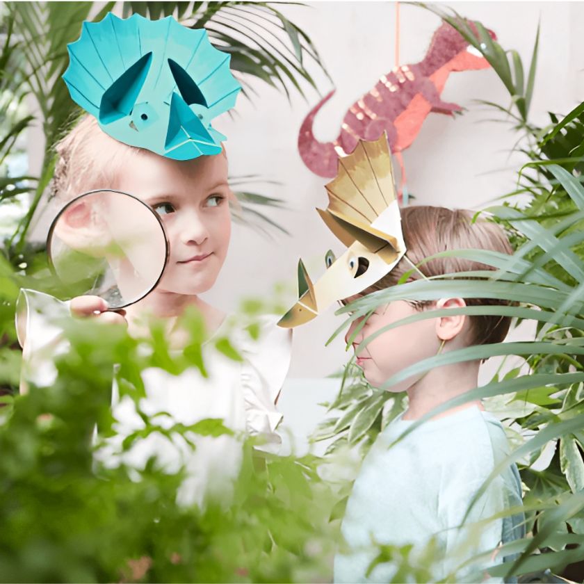 Kids Exploring Garden With Looking Glass And Dinosaur Hats On.