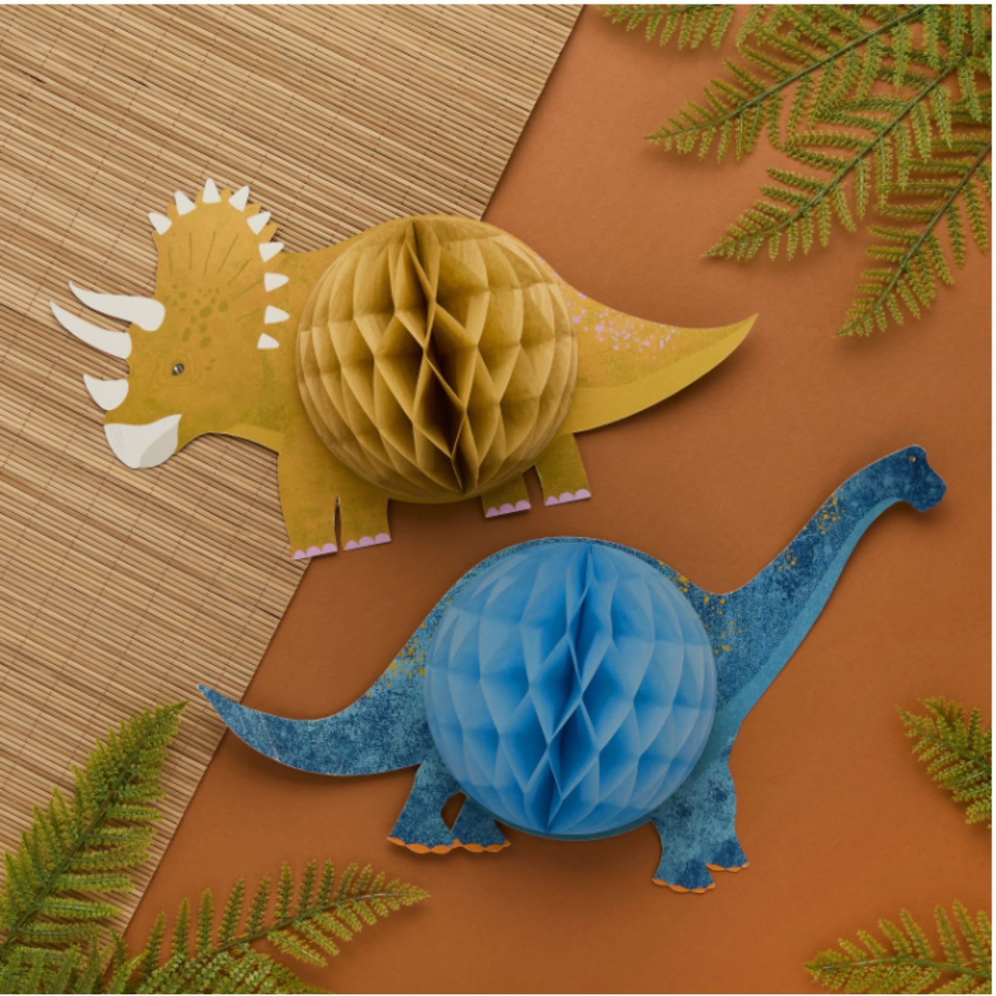Two paper honeycomb dinosaurs, one yellow and one blue, on a brown background with green leaves.