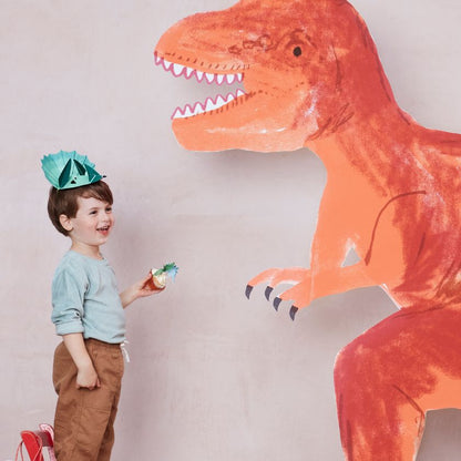 Image of boy at Dinosaur party with Meri-Meri's Dinosaur hat on in front of huge cut out orange Dinosaur.