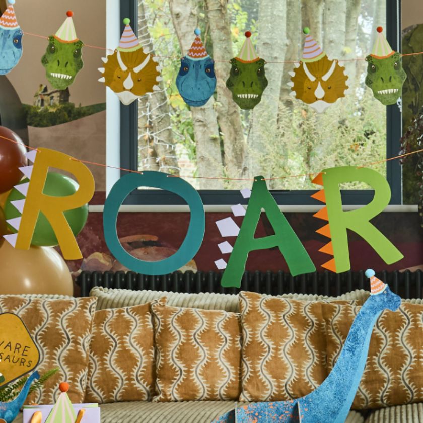 Dinosaur-themed party decorations with 'ROAR' letters and balloons in a living room.
