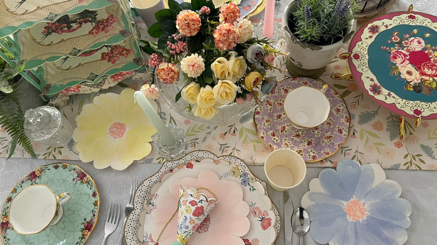 tea party table setting with colourful flower shaped plates, cups, cake stands and party hats