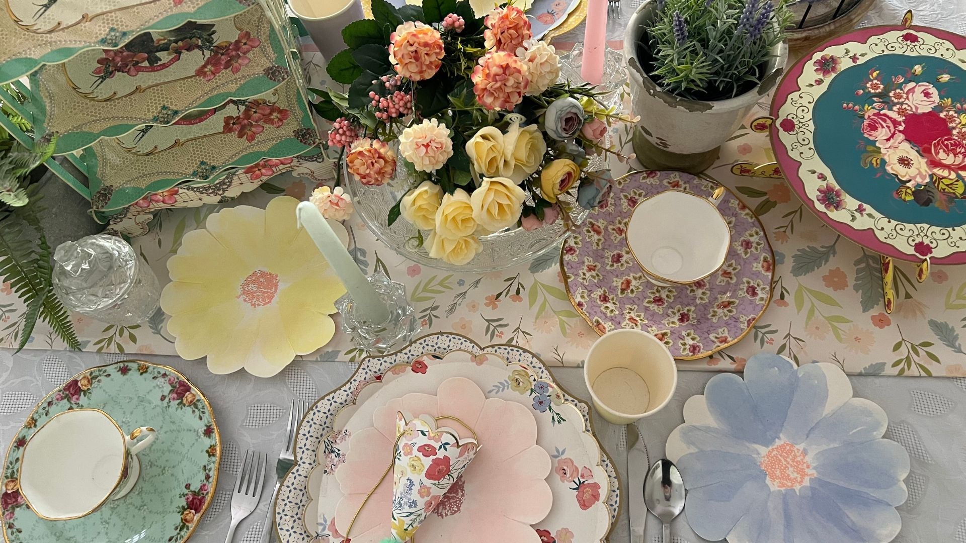 tea party table setting with colourful flower shaped plates, cups, cake stands and party hats