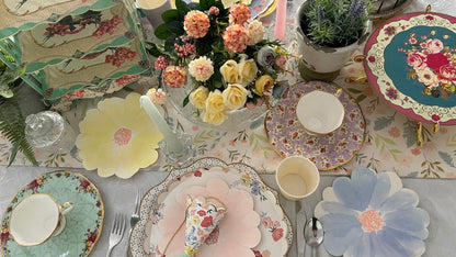 tea party table setting with colourful flower shaped plates, cups, cake stands and party hats